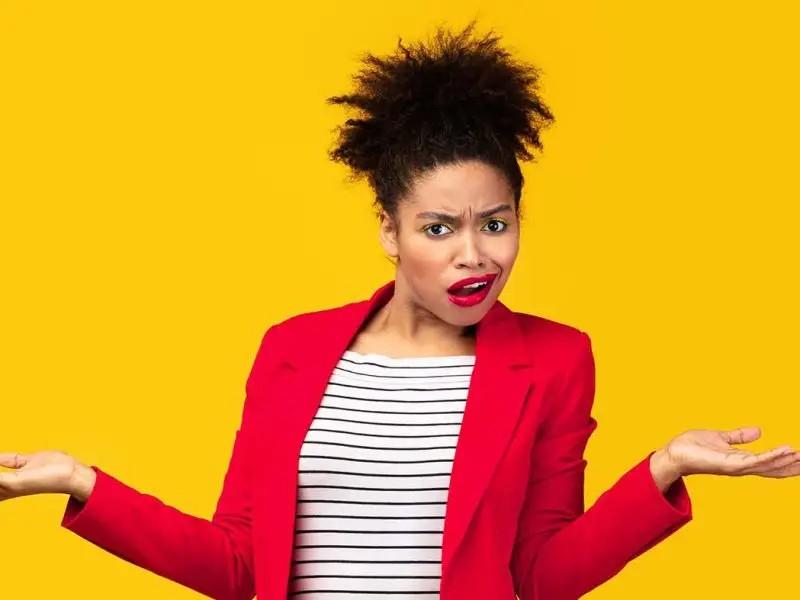 Why Giving Clients What They Want Isn't Always the Best Strategy - this image shows a bright yellow background with an attractive lady in the foreground, she is wearing a bright red blazer and has her arms extended from the elbows out to each side as if she is shrugging and has an confused look on her face