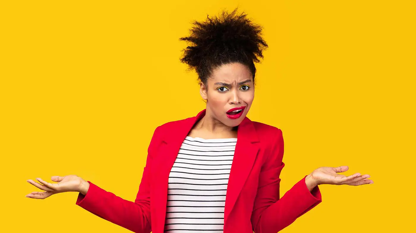 Why Giving Clients What They Want Isn't Always the Best Strategy - this image shows a bright yellow background with an attractive lady in the foreground, she is wearing a bright red blazer and has her arms extended from the elbows out to each side as if she is shrugging and has an confused look on her face