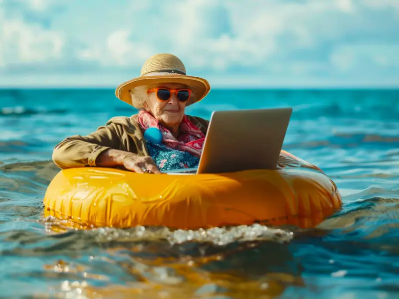 Renewing Domain Names - this image is whimsical and shows an older lader in the sea in a yellow blow up ring working on a laptop.