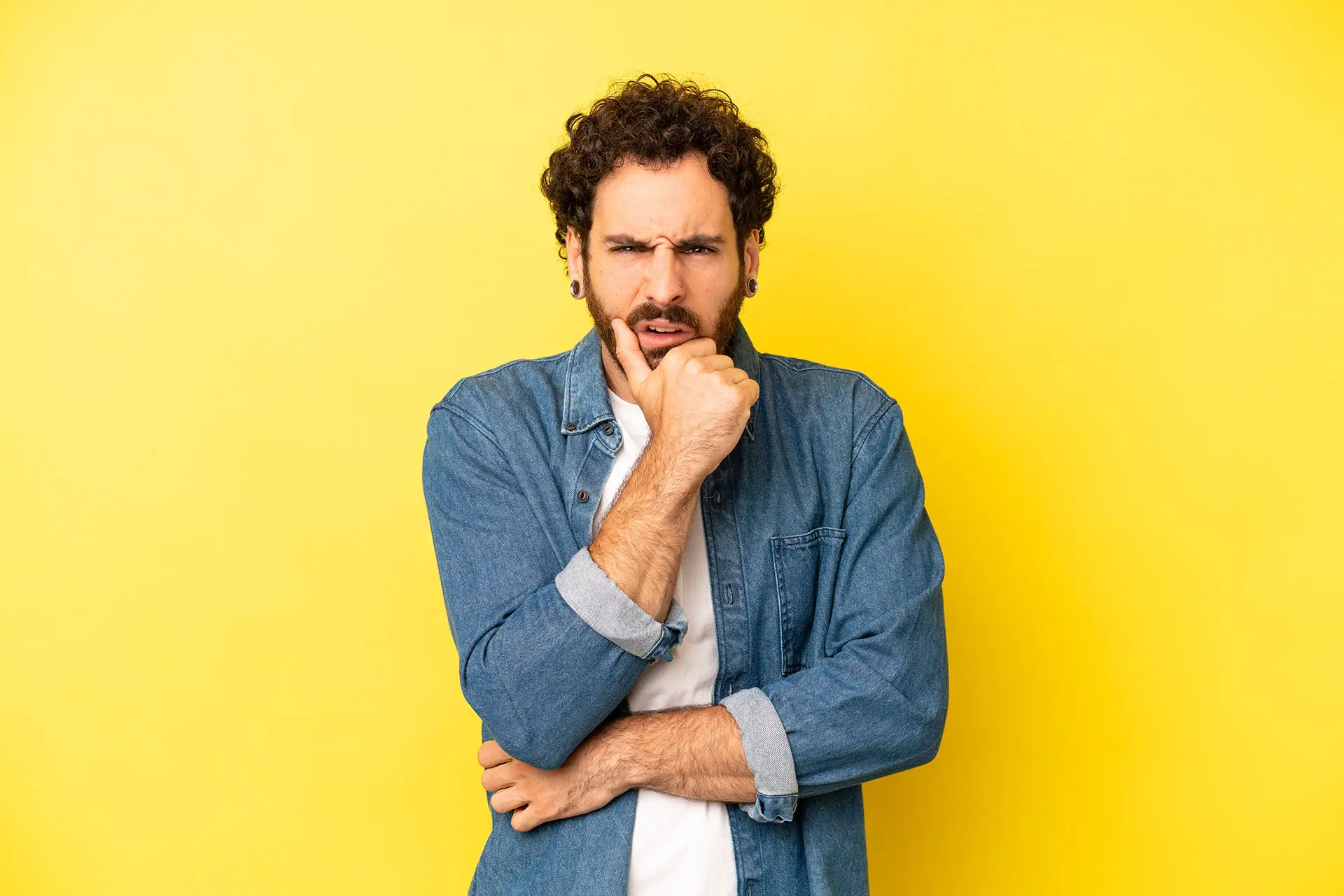 What Are Landing Pages? This image shows a bright yellow background with a confused man in the foregraound with one arm across his body and the other raised with his hand cupping his chin, he has a thoughtful expression on his face