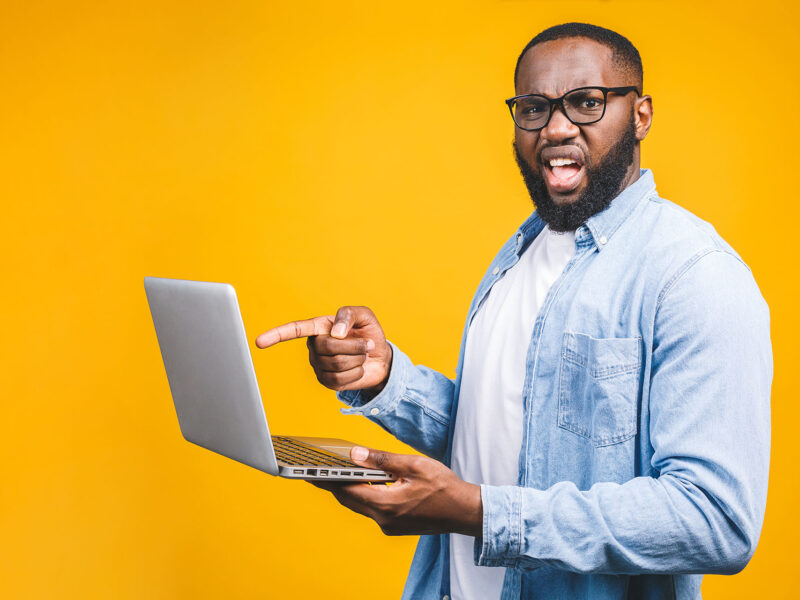 How to Clear Your Browser Cache - this image shows a bright yellow background with a man in glassess pointing at his laptop screen looking frustrated